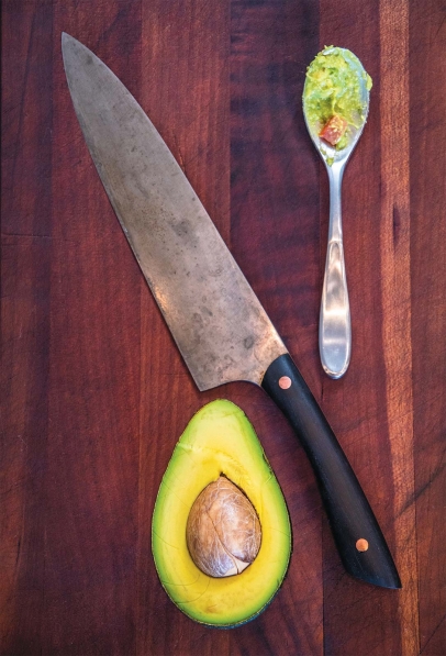 Avocado with knife and spoonful of guacamole